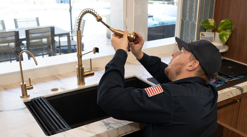 Paramount's plumber repairing a kitchen faucet in a modern kitchen.