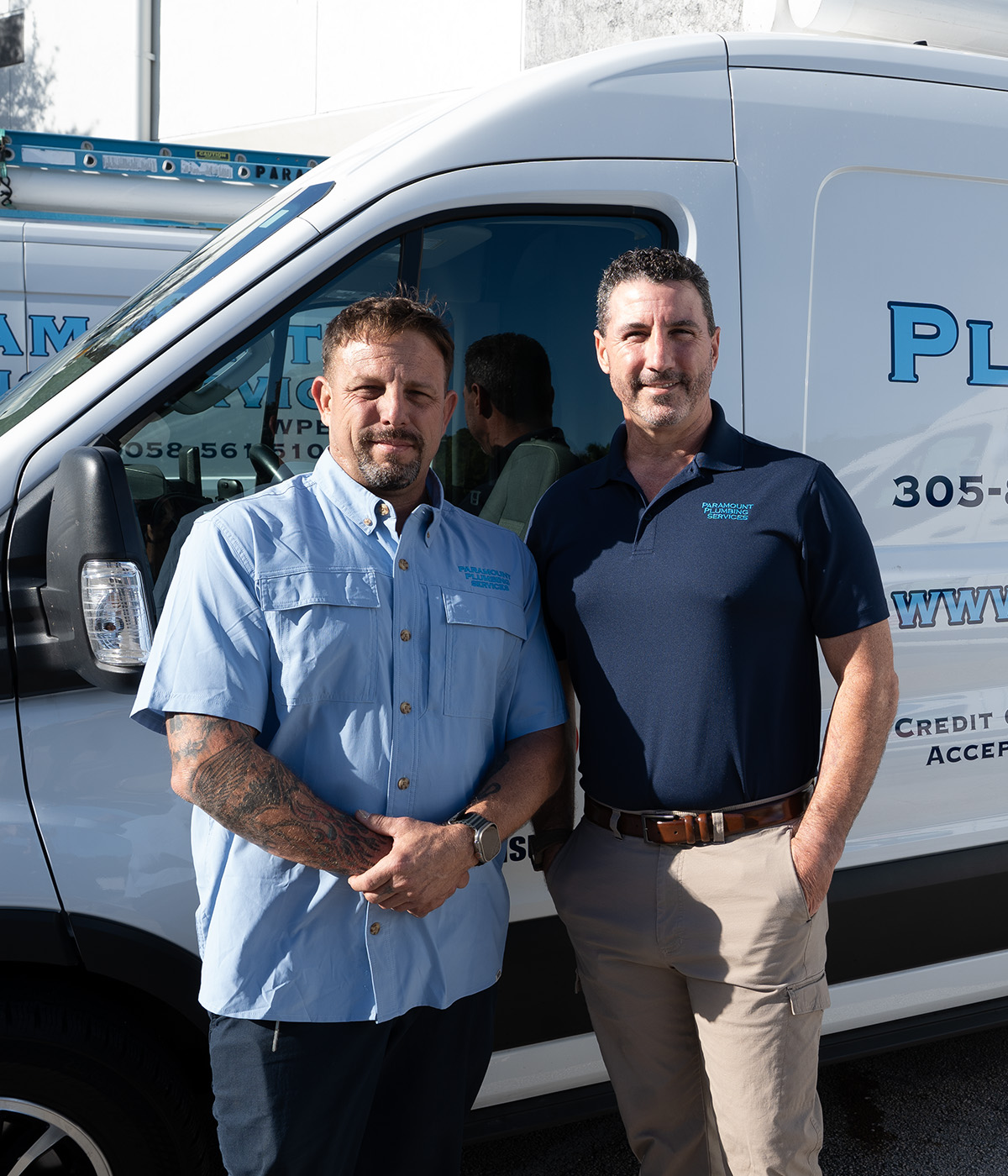 Paramount plumbers in work uniforms stand confidently in front of their service van