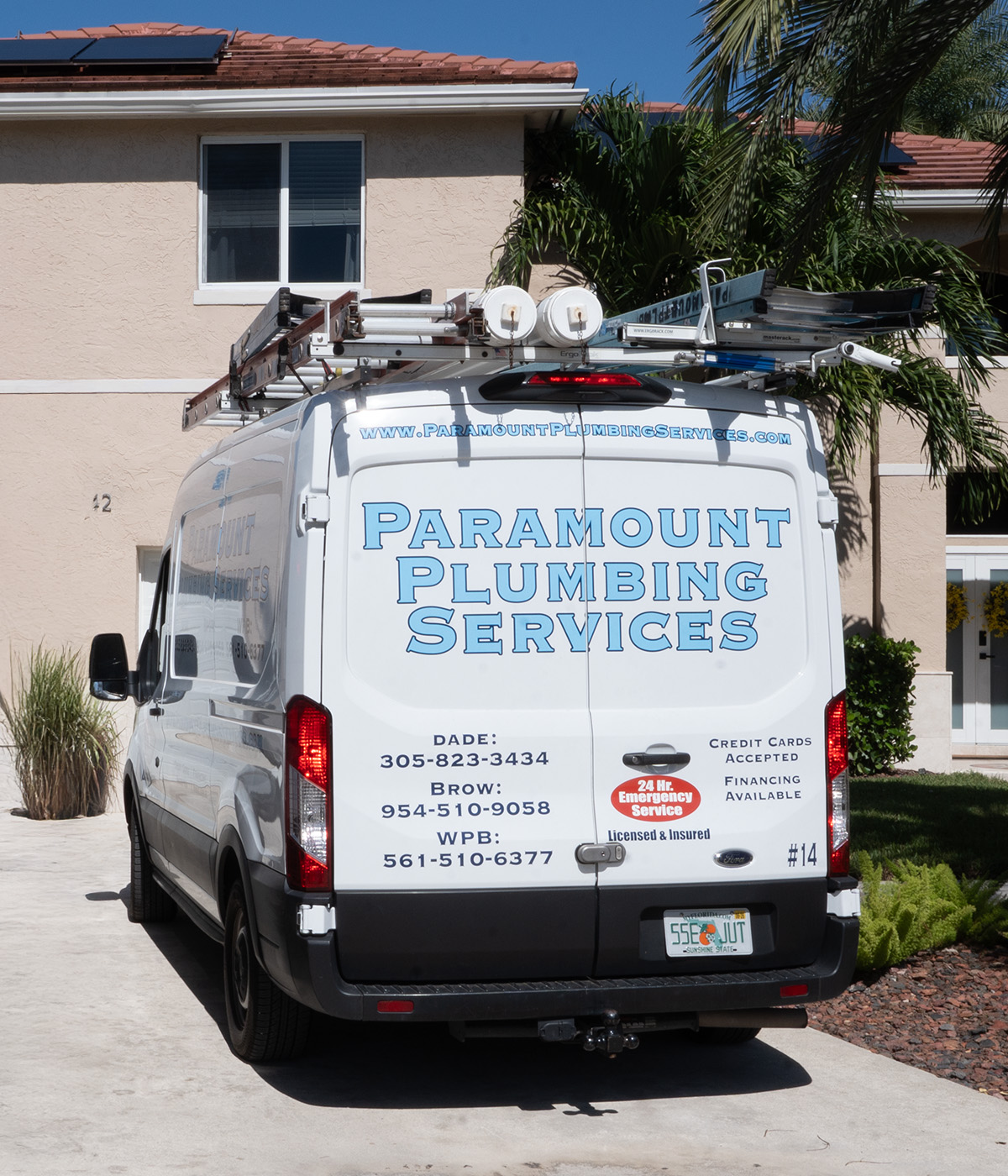 A white plumbing service van parked outside a house, featuring "Paramount Plumbing Services" and contact info on the back.