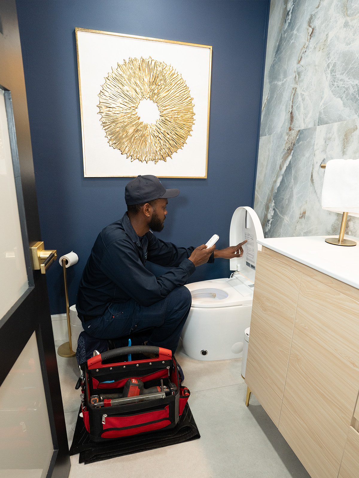 Paramount's plumber inspects a modern toilet in a stylish bathroom, tools organized in a red and black bag beside him.