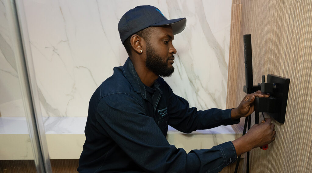 paramount's plumber in a blue uniform adjusts a black wall fixture, working on installations against a marble-like background.