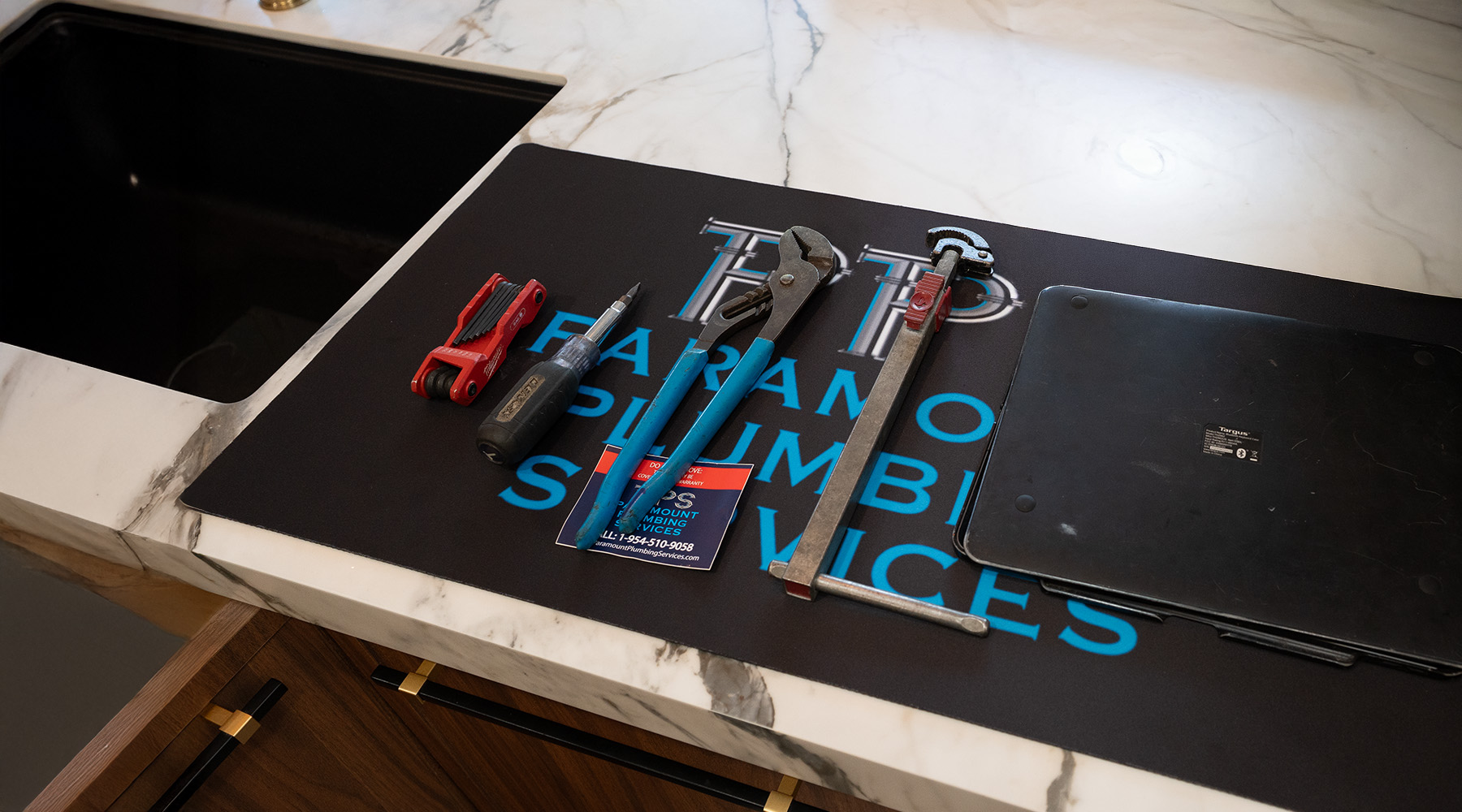 paramount plumbing services branded work mat with adjustable wrench hex keys and screwdrivers on white marble counter