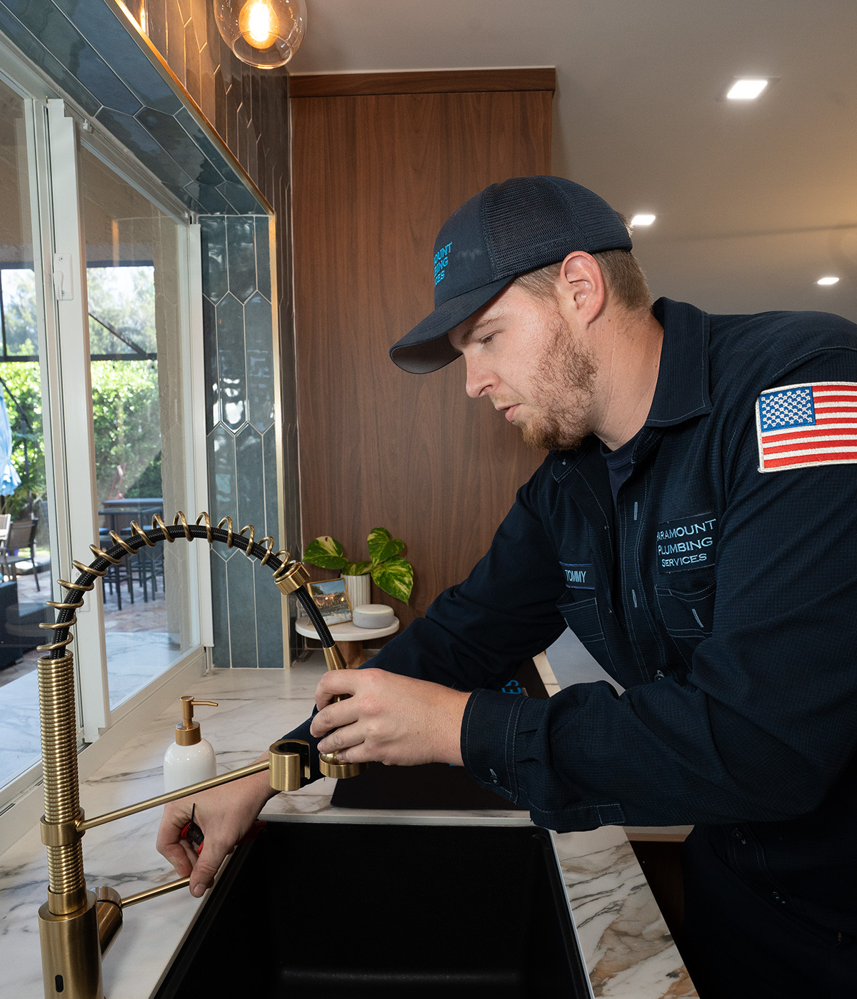 A plumber adjusts a modern gold faucet at a kitchen sink