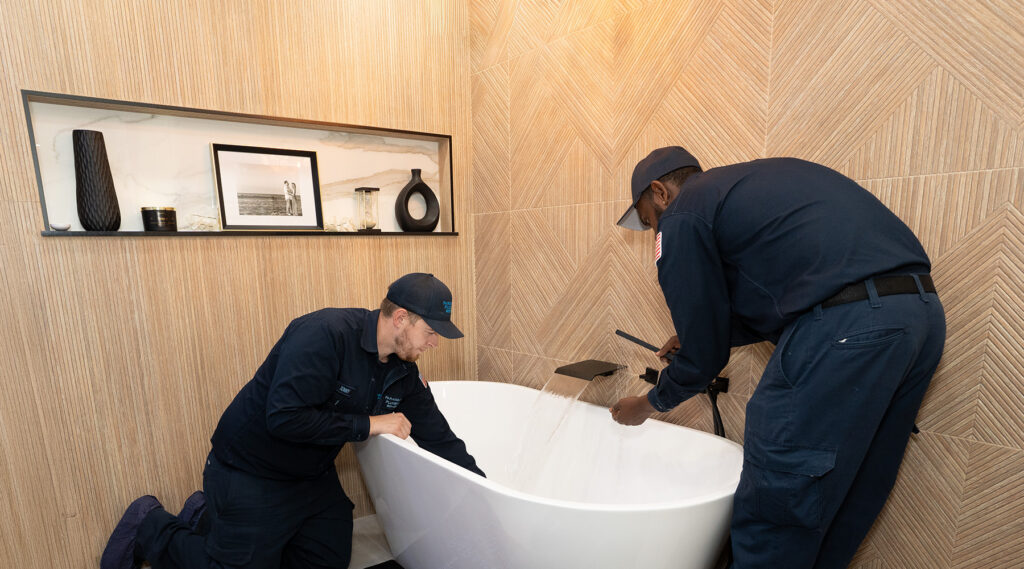 Two Paramount's plumbers in uniforms are inspecting a modern bathtub, with water flowing from the faucet