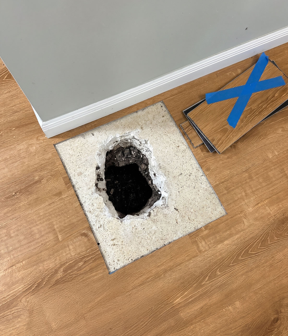 Access hole cut into vinyl plank flooring for slab leak repair