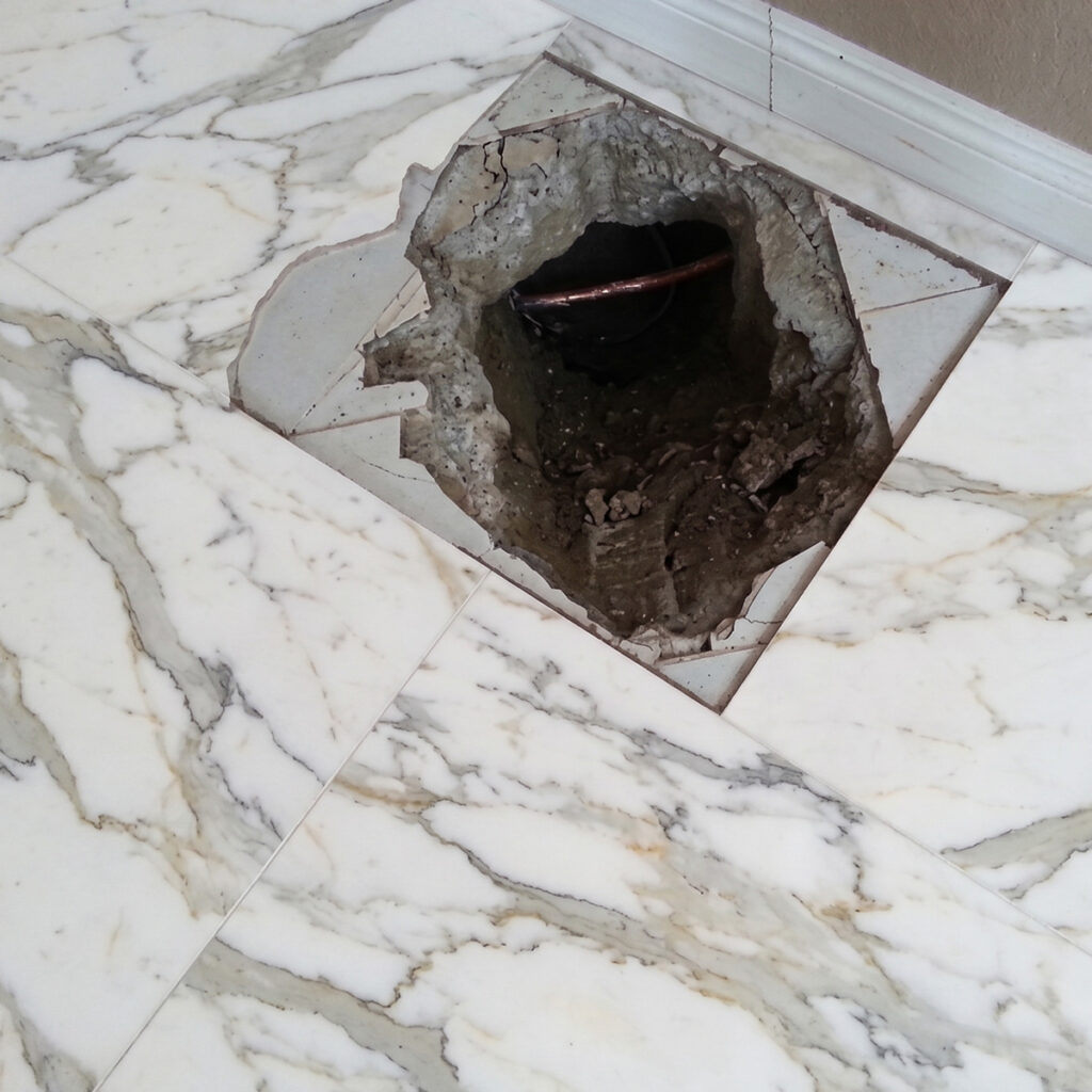 Broken tile floor exposing copper water pipe access hole