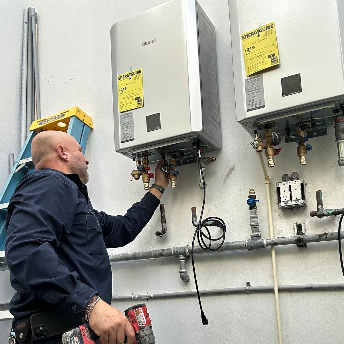 Paramount plumber working on two Rinnai tankless water heaters on exterior wall