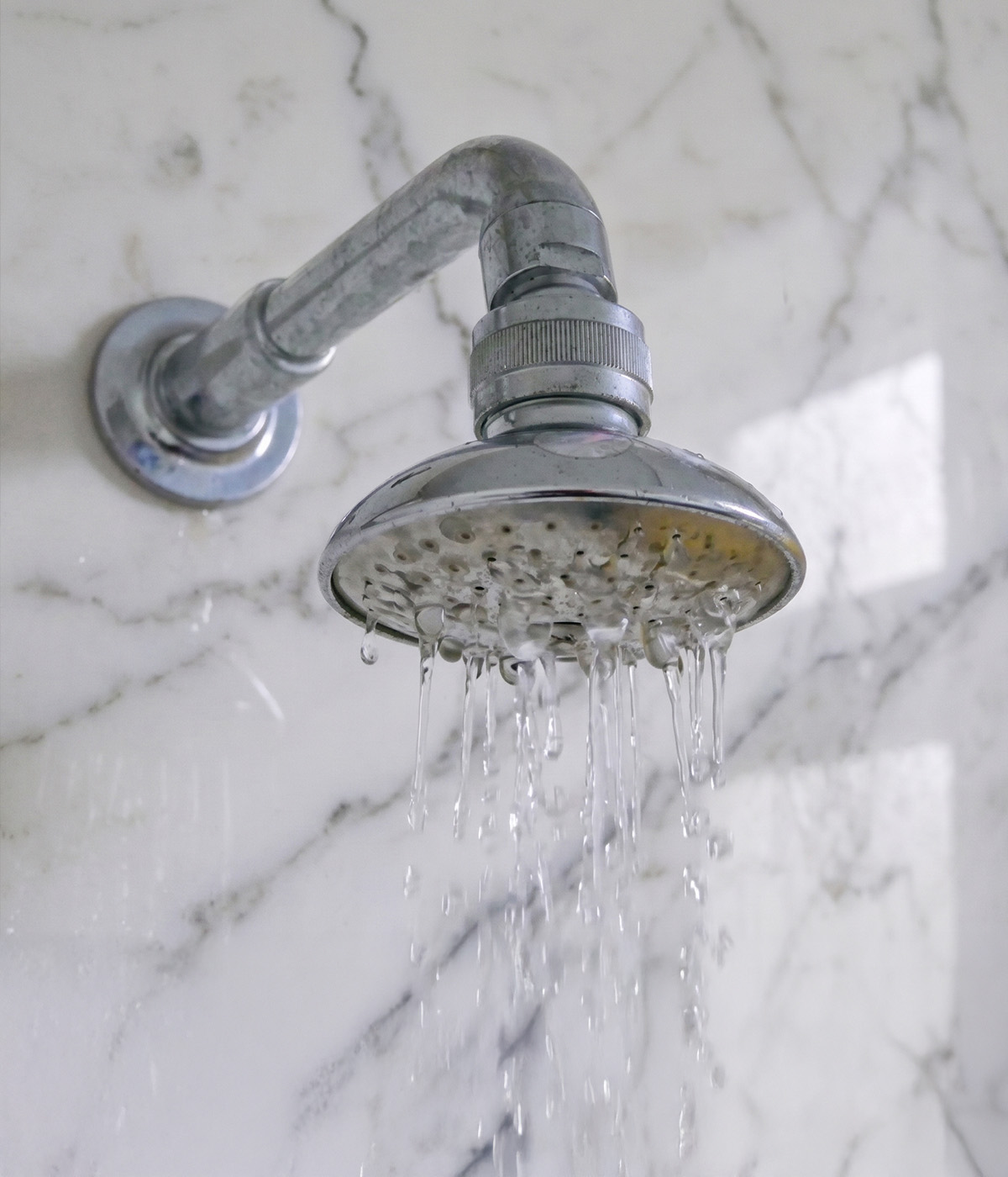 Chrome showerhead running water against marble tile bathroom wall